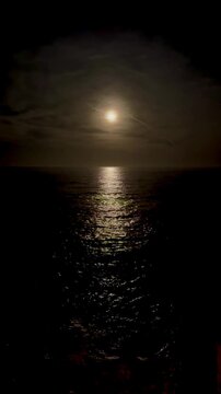 full moon reflecting on the calm sea. Dark sky with a few clouds. Romantic atmsophere. Can also work for halloween
