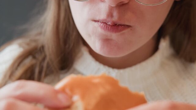 Tight frontal view of lower face and both hands gripping glossy sesame bun near mouth, with lips pursed and jaw tense, capturing anticipation before bite in soft indoor light, with burger, mouth