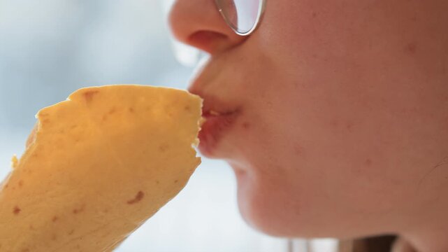 Tight close-up captures lower face moving toward handheld golden pastry, lips pursed and pastry edge near mouth, with flaky crumbs, warm light, and subtle sensory anticipation, with pastry, mouth