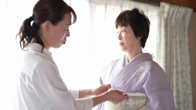 An assistant adjusts the front of a pale patterned obi worn over a lavender kimono. Japan, April 19, 2025, spring.
