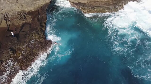 Aerial drone footage showing person swimming in natural ocean rock pool surrounded by rugged cliff formations.