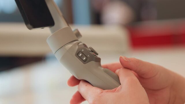 Close-up of hands holding light-gray handheld device while thumbs and fingers press buttons, rotate dials, and manipulate directional pad on control panel; motion shows active adjustment