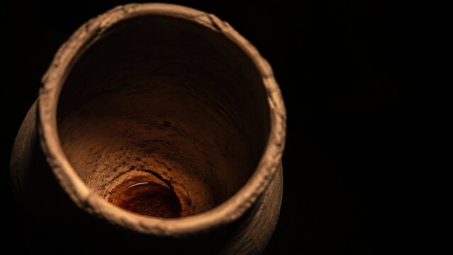 Ancient clay jug with red wine inside on dark black background. Miracle of Jesus turning water into wine at wedding in Cana of