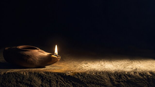 Ancient clay oil lamp burning with flame on old stone table in darkness. Biblical times light in dark night. Faith and hope concept. Miracle of Jesus at wedding in Cana of Galilee. Copy space