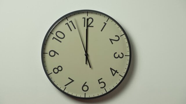 Analog clock hands showing 12:00 and passing time. Modern white wall clock time lapse on white wall.