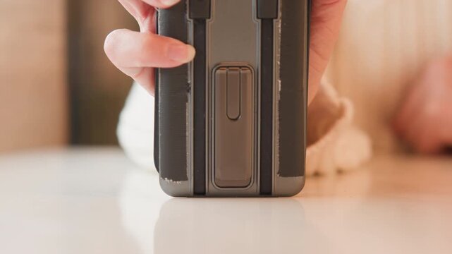 Close view of hands steadying compact stapler on pale wood tabletop while index finger applies downward pressure to metal staple area, showing simple office action, product detail, and focused