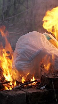 White plastic garbage bag full of waste burning in an open fire, melting and releasing thick, toxic smoke, highlighting the serious issue of environmental pollution and hazardous fumes