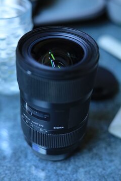 Black camera lens standing upright on a textured blue surface with photography