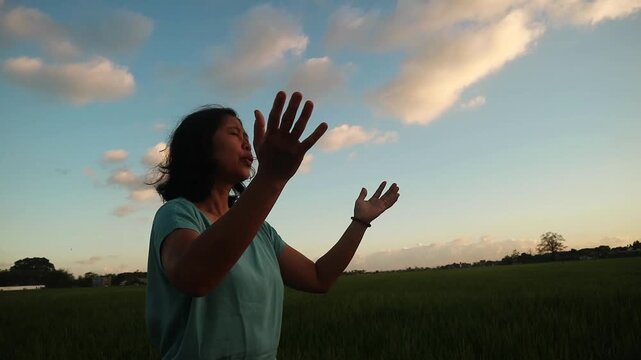 A woman standing in a field with her hands raised towards the sky at sunset. outdoor wellness activity