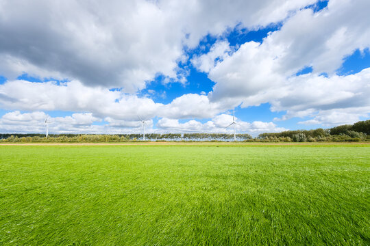 Panoramic rural field and meadow with green grass under a sky with clouds. Small wind turbine visible in the background nature environment.