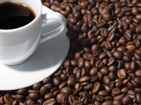 White espresso cup placed on roasted coffee beans texture close-up