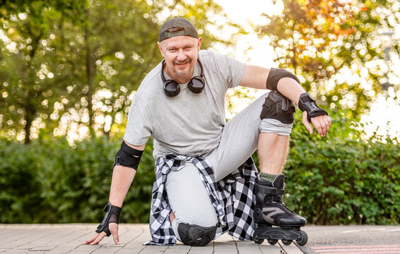 Active man wears protective gear and inline skates while resting on paved park ground at sunset