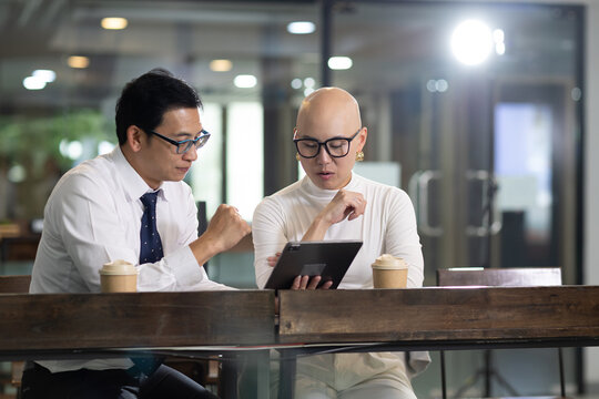 Two Asian business professionals review data on tablet during office meeting, discussing project and sharing ideas over coffee working together on business planning and strategy. meeting brainstorm.