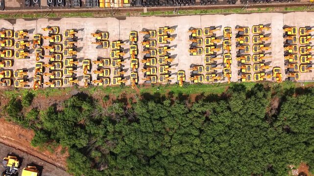 Green vegetation beside rows of yellow construction machinery at heavy equipment manufacturing unit industrial