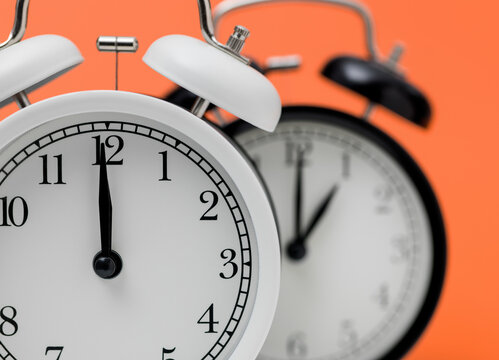 Daylight saving time change concept with white alarm clock at twelve o'clock