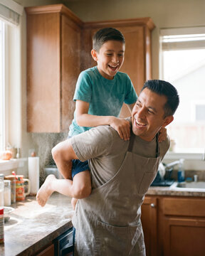 Spirited father giving son piggyback ride in sunlit home kitchen with warm natural light