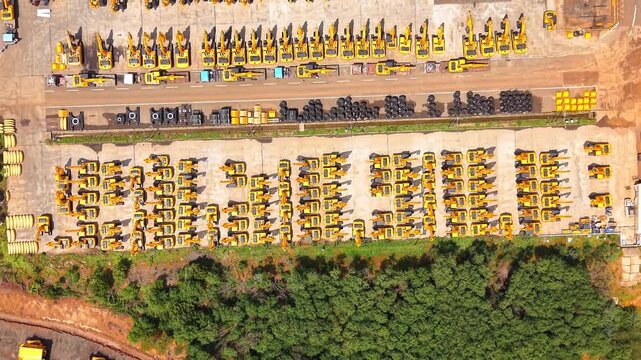 Rows of yellow construction machinery beside green vegetation at heavy equipment manufacturing plant industrial