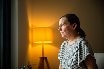 Mature woman reflecting quietly while sitting on a sofa at home. Decision making, personal...