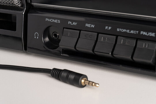 Close-up of a headphone jack, audio plug and physical buttons on a vintage cassette player. The wired connection and tactile controls recall a more hands-on way of listening to music
