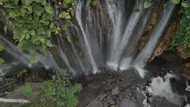 Stunning Aerial View of Waterfall Surrounded by Lush Greenery and Rocks in Nature's Embrace