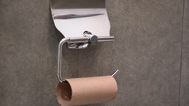Empty toilet paper roll holder close up, brown cardboard core tube on chrome metal hanger inside bathroom restroom, running out of household tissue supply conceptual minimal apartment background.
