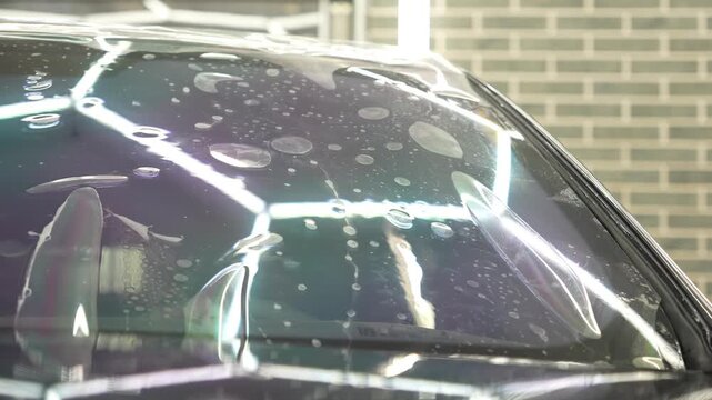Hands of a man glue a clear protective film against scratches on a car windshield close up. This is an athermal window tint wrap. Worker installs a chameleon vinyl sheet on an automobile glass. 