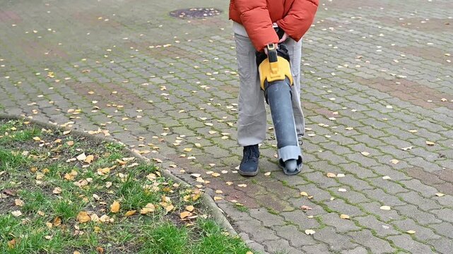 Teenage girl using a leaf blower to clear fallen leaves in autumn. Seasonal yard and garden cleanup, outdoor work, property maintenance, and fall home care.
