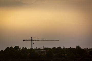 Fototapeta premium Construction Crane Silhouetted Against a Golden Sunset Sky in Moraira, Costa Blanca, Spain