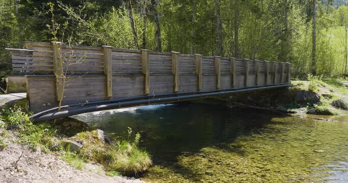 Wooden footbridge crossing the Seebach river on its way to Lunzer See, Lower Austria. Clear water flows beneath the bridge, surrounded by lush spring forest, with the sound of a nearby small waterfall