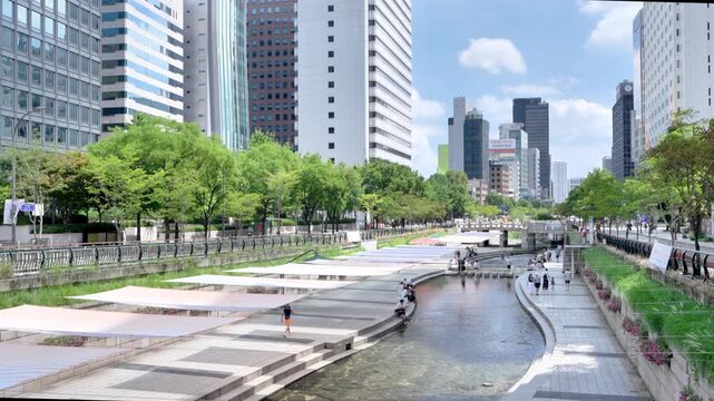 4K video of Cheonggyecheon stream flowing through Seoul downtown with tourists and modern skyscrapers on a sunny summer afternoon