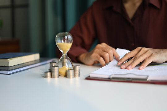 Coin stacks and sand clock on the table. Growing of income, saving or return investment through time. Time and money concept.