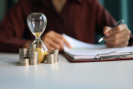 Coin stacks and sand clock on the table. Growing of income, saving or return investment through time. Time and money concept.