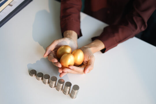 Rising stack of coins on the table and golden eggs on businessman's hand. Concept for financial planning and investment return.