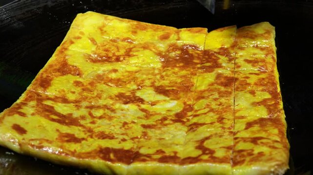 Egg dish being sliced on hot griddle