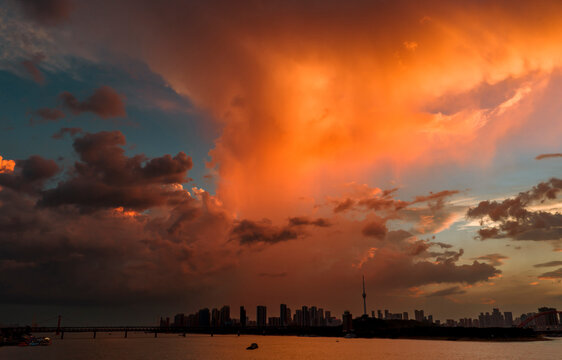Dramatic sunset over the Wuhan skyline and Yangtze River. This fiery sky features "virga" phenomenon, where falling rain catches golden light, creating a stunning illusion of burning clouds.	
