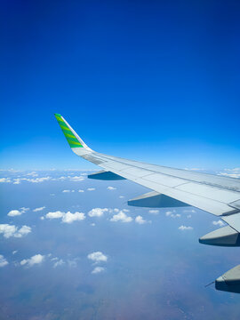 Airplane wing view from window seat, bright blue sky with fluffy white clouds below, green-yellow winglet, flying high above the horizon. Perfect travel and aviation scene, portrait view. 