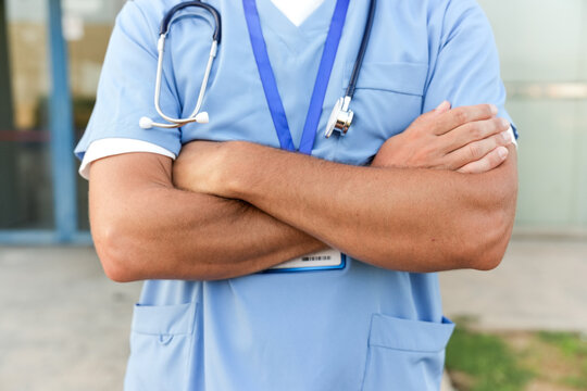 Healthcare worker, doctor or nurse, standing confidently with arms crossed, wearing blue scrubs and stethoscope