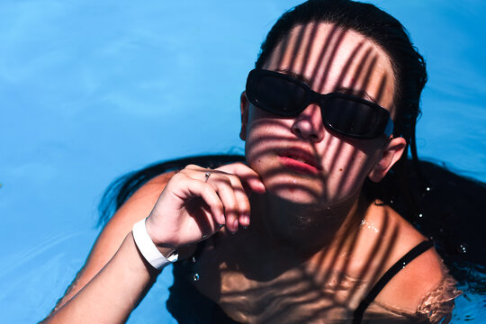 Woman in swimming pool with dramatic shadow patterns, blue water and sunlight reflections, woman and water summer lifestyle concept, relaxation mood, poolside leisure, elegant vacation atmosphere