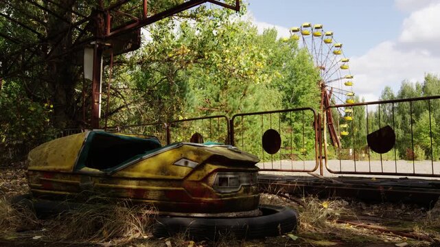 Abandoned bumper car in Pripyat amusement park with ferris wheel in background.