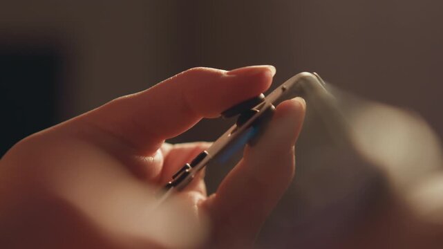 Tight close view of hands holding metal nail clipper to trim fingernail edge, with lever pressed down, jaws aligned to curved nail, and small debris visible during careful personal care
