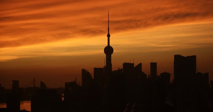 Morning sun rises and lights up the dawn sky behind the silhouette of Oriental Pearl Tower and Pudong skyscrapers in Shanghai, captured in timelapse