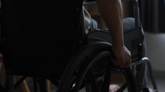 Close up of senior man hand operating wheelchair wheel for indoor mobility.