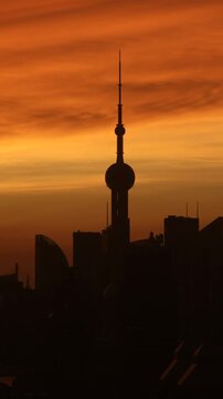 Orange morning sky brightens into daylight behind the dark silhouette of Oriental Pearl Tower and Pudong skyscrapers in Shanghai, captured in vertical timelapse