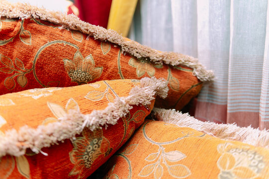 Close-up of orange patterned fabric cushions with fringe details stacked on a sofa indoors.
