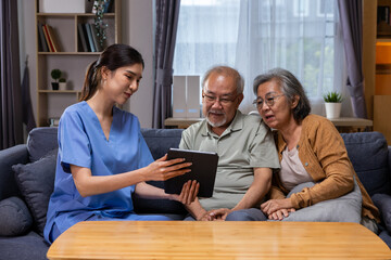 Obraz premium Asian nurse elderly couple tablet living room healthcare conversation Asian nurse helps elderly couple use tablet comfortable living room, creating supportive home care moment filled with trust