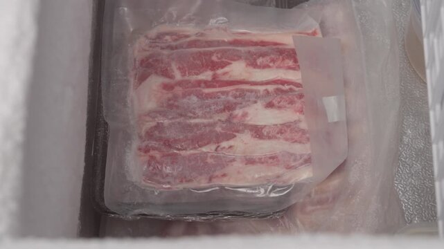 Person removing frozen raw beef strips from freezer compartment for meal preparation.