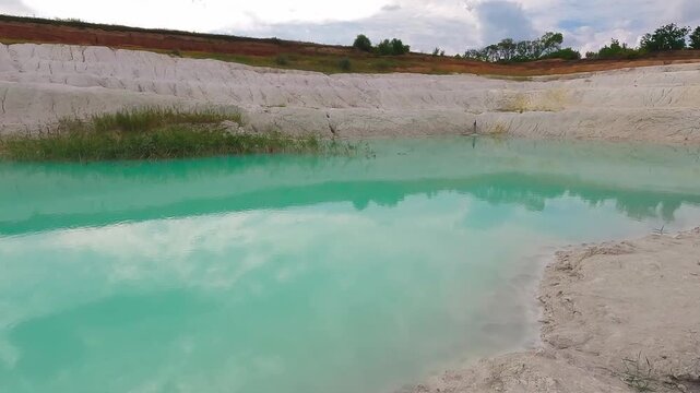View across the white clay shoreline and turquoise water of an abandoned kaolin quarry.