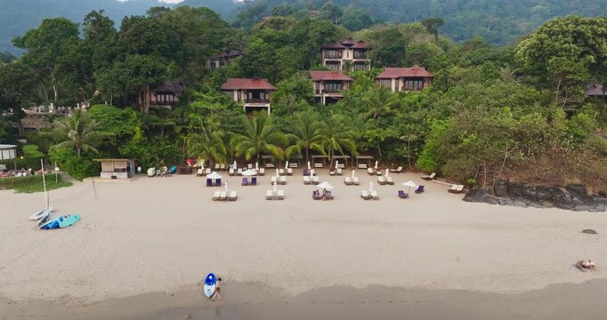 Koh Lanta is a beautiful sandy beach lined with lounge chairs and umbrellas. Featuring luxurious resort bungalows nestled among lush tropical vegetation and palm trees in Thailand. Aerial drone flight