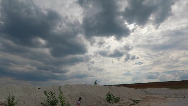 Aerial view of an abandoned kaolin clay quarry with bright white mineral deposits, barren terrain and dramatic cloudy sky.