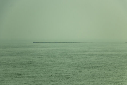 Remote sand island sitting in calm sea under hazy green sky horizon.